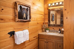Ein Badezimmer im Holzblockhausstil mit einem Bärenbild, einem Waschbecken, einem Spiegel und einem Handtuchhalter.