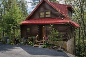 Eine Blockhütte mit rotem Dach, hölzernen Stufen, die zum Eingang führen, und einem Steinfundament.