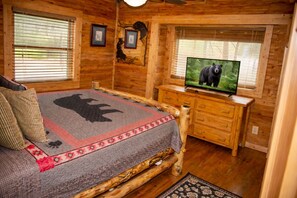 Ein Blockhausszimmer mit Bett, Fernseher, Holzwänden und gerahmten Bildern.