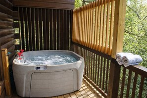 Ein Whirlpool auf einer Holzdiele mit Holzzaun und Bäumen im Hintergrund.