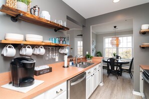 Una cocina moderna con armarios blancos, cafetera y comedor con mesa y sillas.