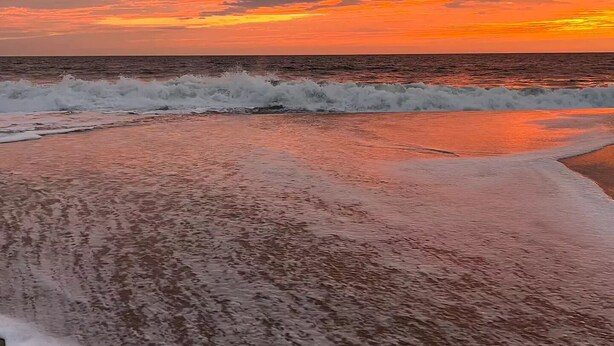 Une plage avec des vagues et un ciel au coucher du soleil.