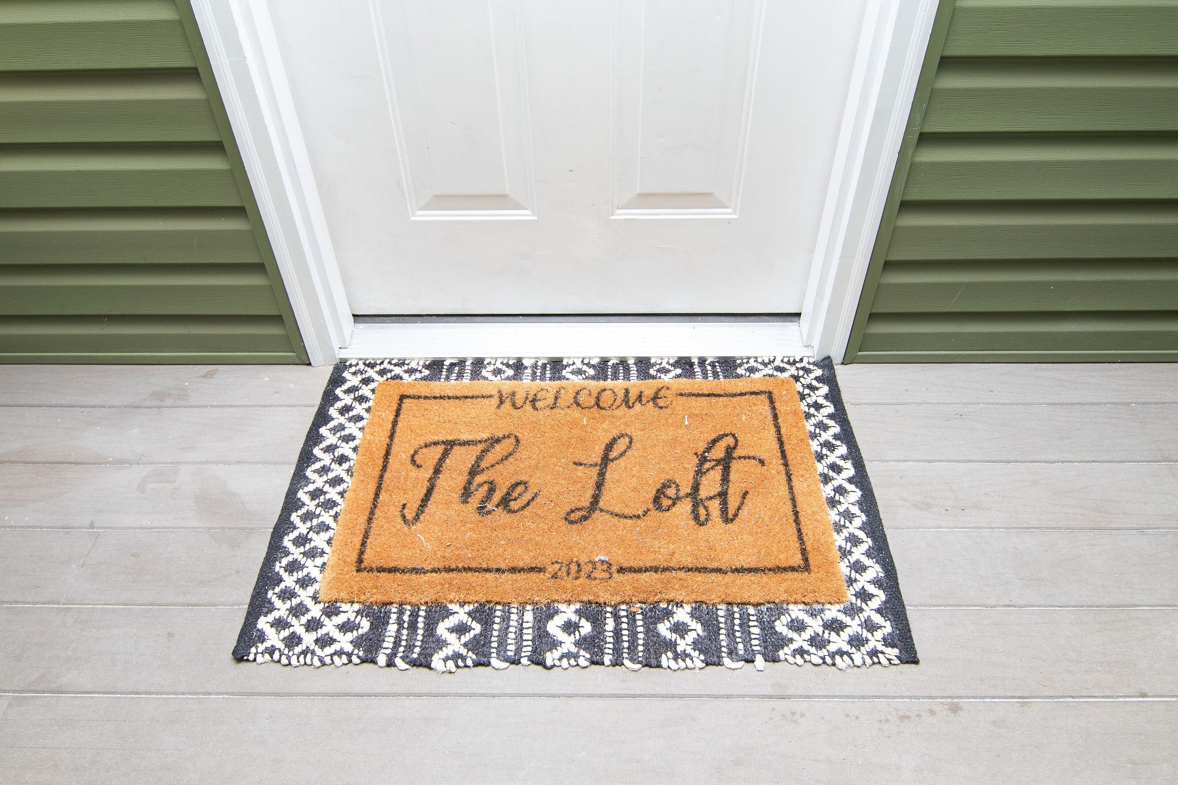 Un paillasson avec l’inscription « Bienvenue au Loft 2013 », placé devant une porte dont le revêtement extérieur est vert.
