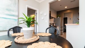 Un coin repas avec une table noire, des sets de table en fibres tressées et une plante en pot.