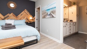 Une chambre à coucher avec un lit, une tête de lit en bois, un miroir fixé au mur et un tableau représentant une scène de plage.