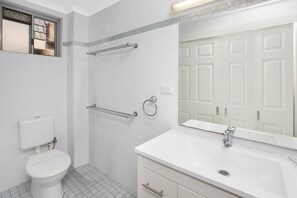 A modern bathroom with a toilet, a shower with grab bars, a sink with a mirror, and a tiled floor. - Forster Lodge 6: 1 BR, 0.5 BA Apartment in Forster, Sleeps 4 (Forster)