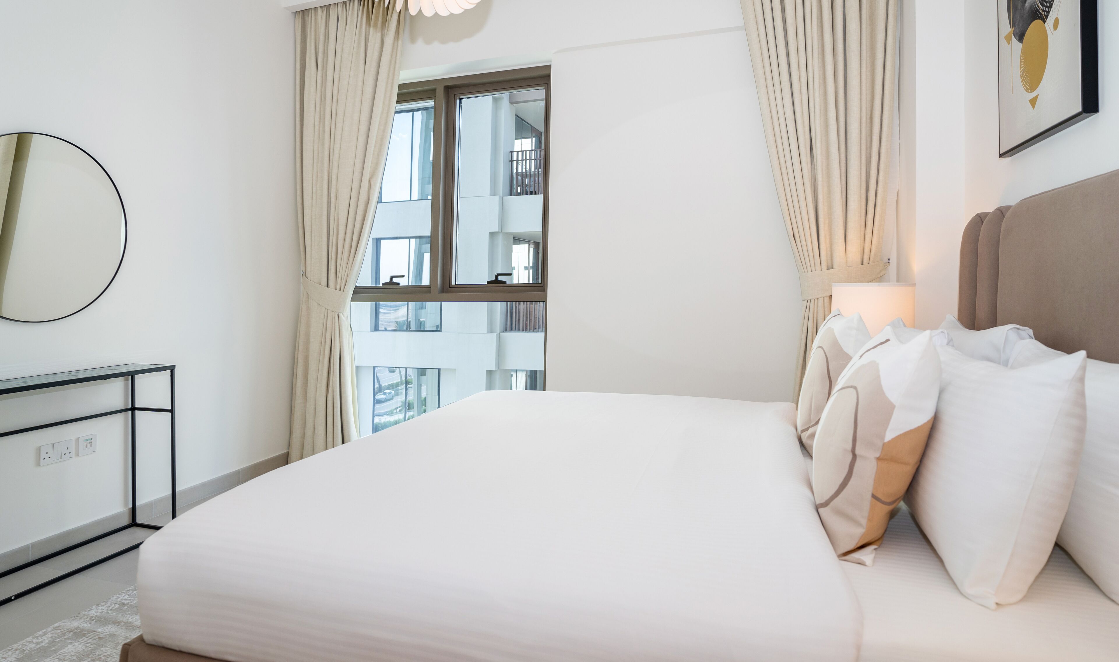 Ein Hotelzimmer mit einem großen Bett, einem Nachttisch, einem Spiegel und einem Fenster mit Vorhängen.