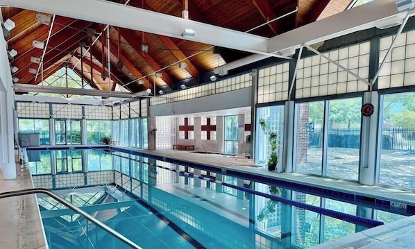 An indoor swimming pool with a wooden ceiling, large windows, and a lifeguard station.