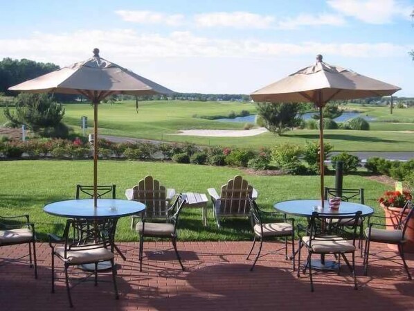 An outdoor patio with two round tables and chairs, two umbrellas, and a view of a golf course. - New Listing * Bear Trap Dunes Resort: Beautiful Vacation House (Ocean View)