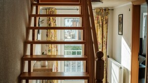 Eine Holztreppe mit Blick ins Freie durch ein Fenster mit blumigen Vorhängen.