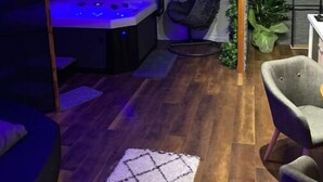 Ein Zimmer mit Holzboden, einer Couch, einem Spieltisch mit Stuhl, einem Hängesessel und einer kleinen Pflanze.