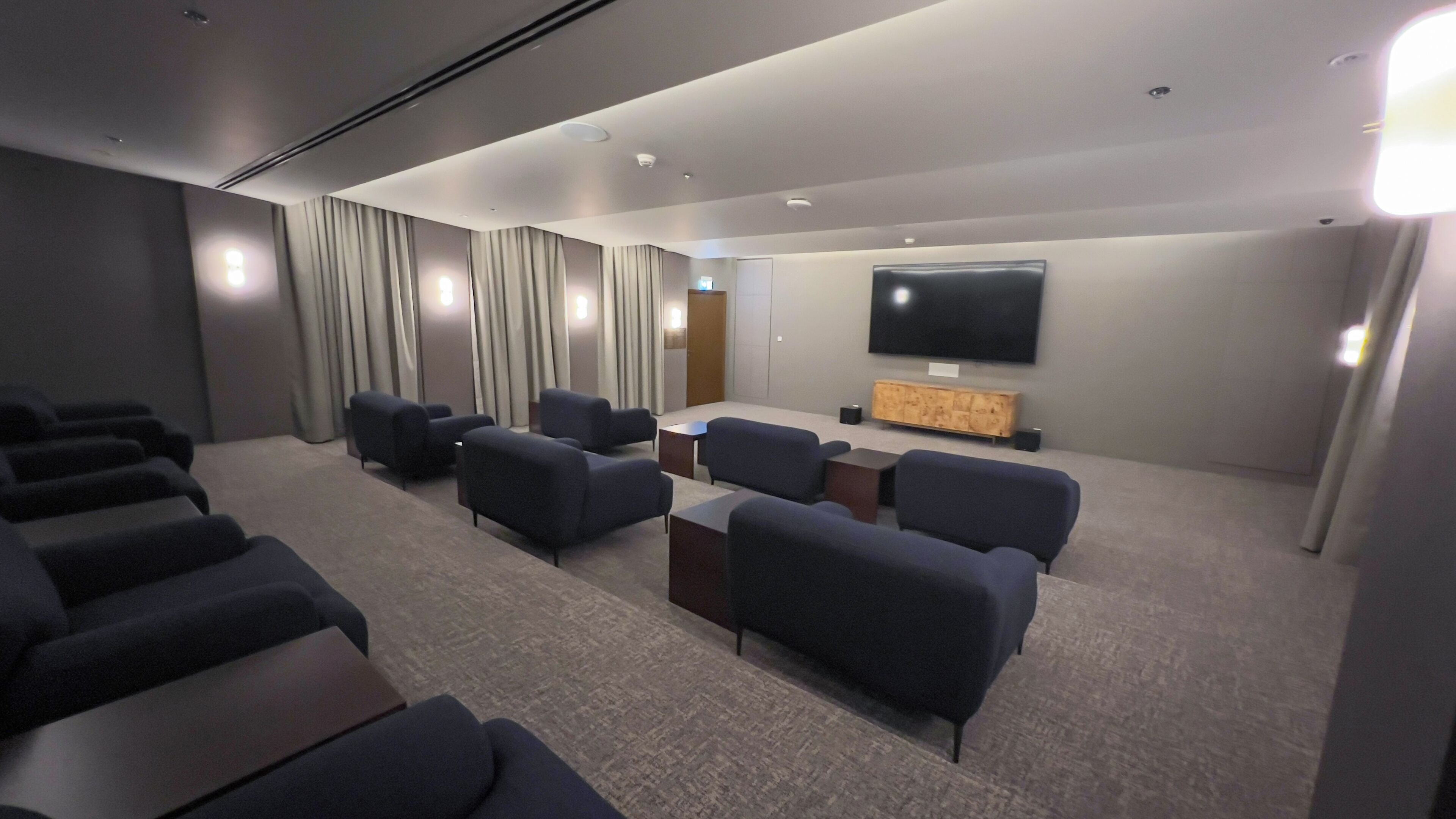 A modern cinema room with rows of seating, a large screen, and a wooden cabinet.