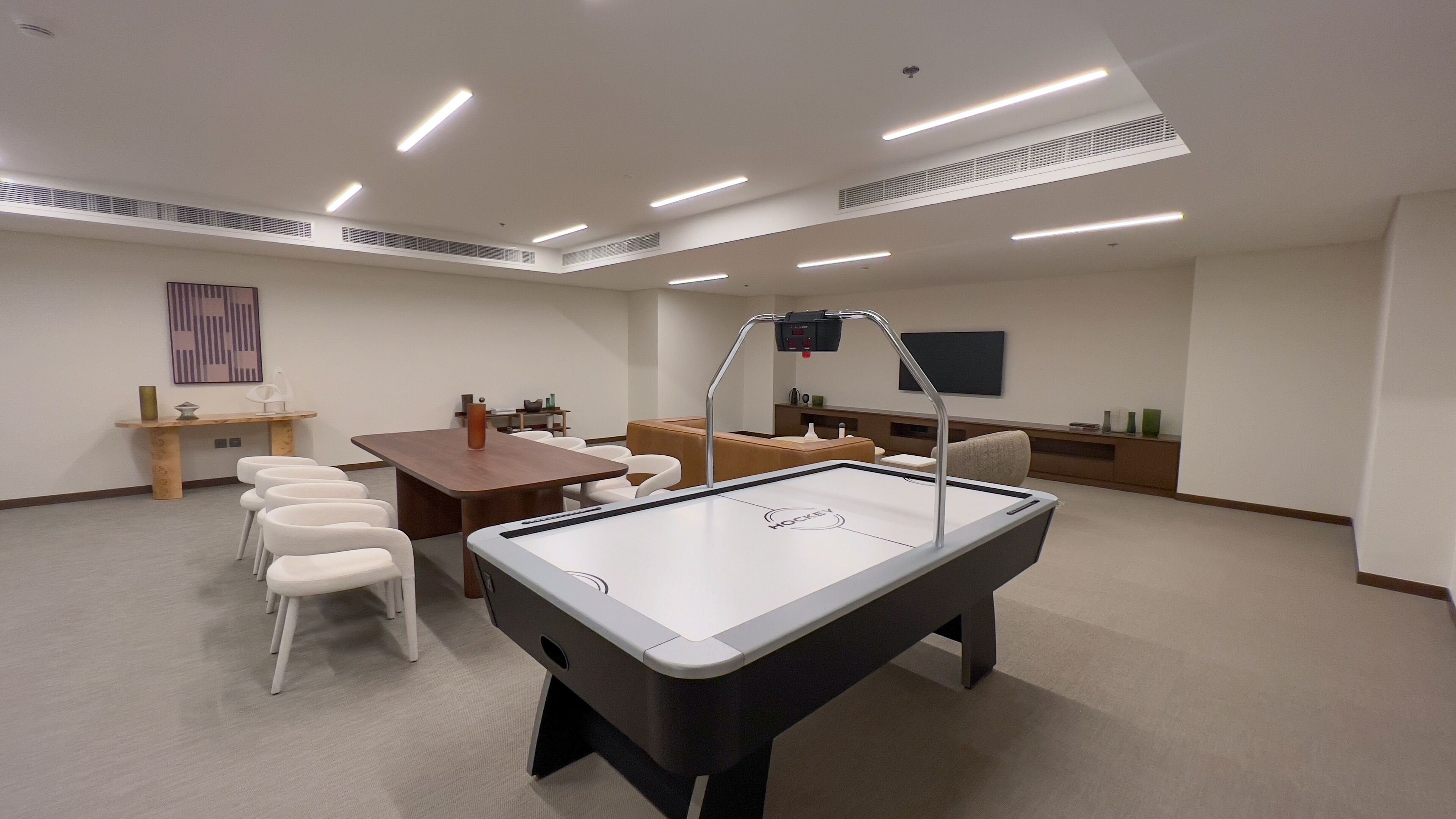 A room with a pool table, white chairs, a wooden table, and a television on the wall.