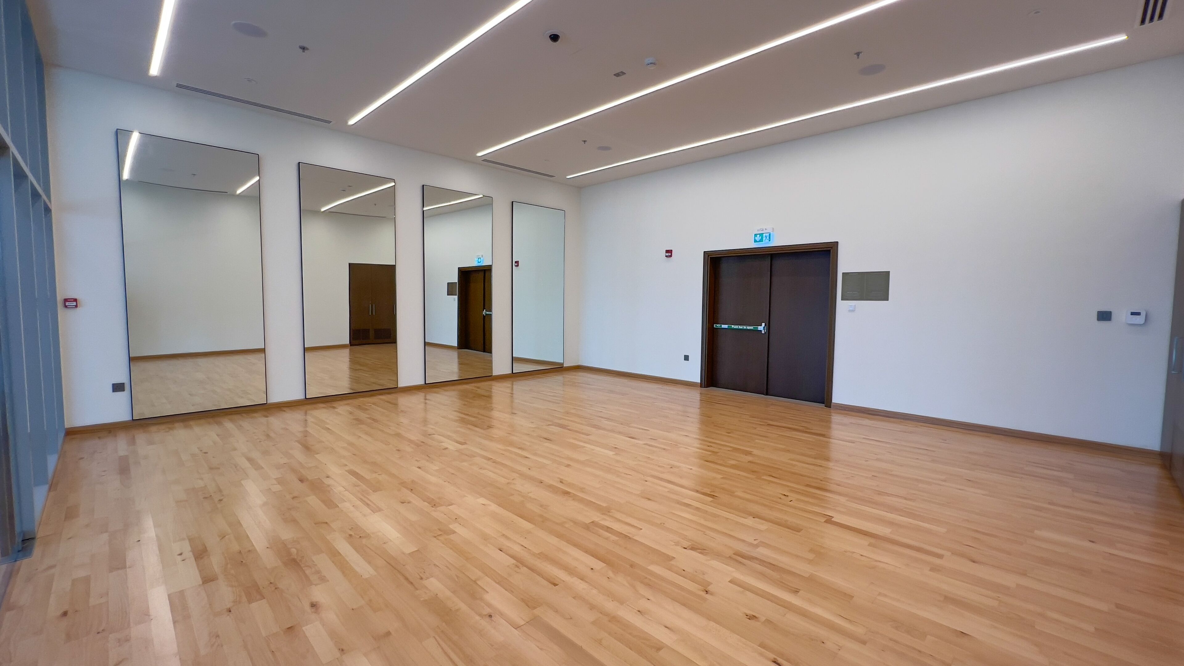A spacious room with wooden flooring, large mirrors, and a door with a sign.
