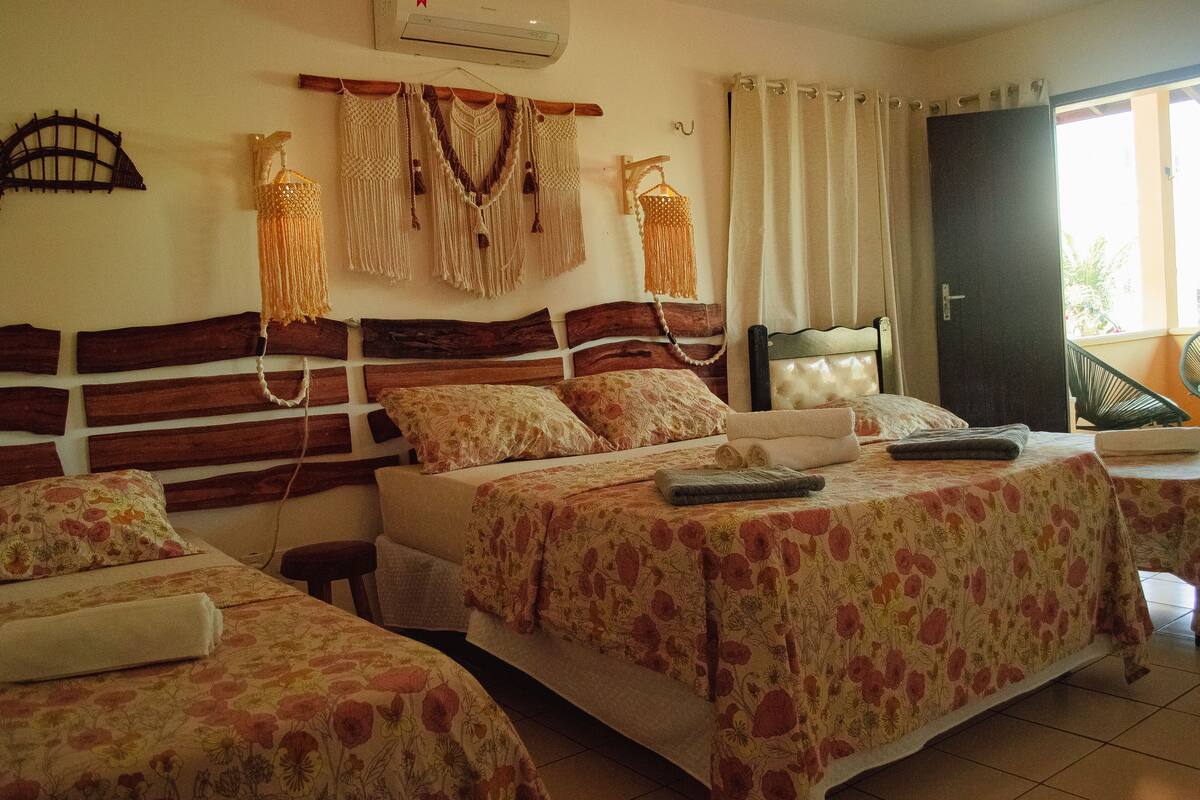 A hotel room with two beds, a wooden headboard, macrame wall decorations, and a view of the outside.