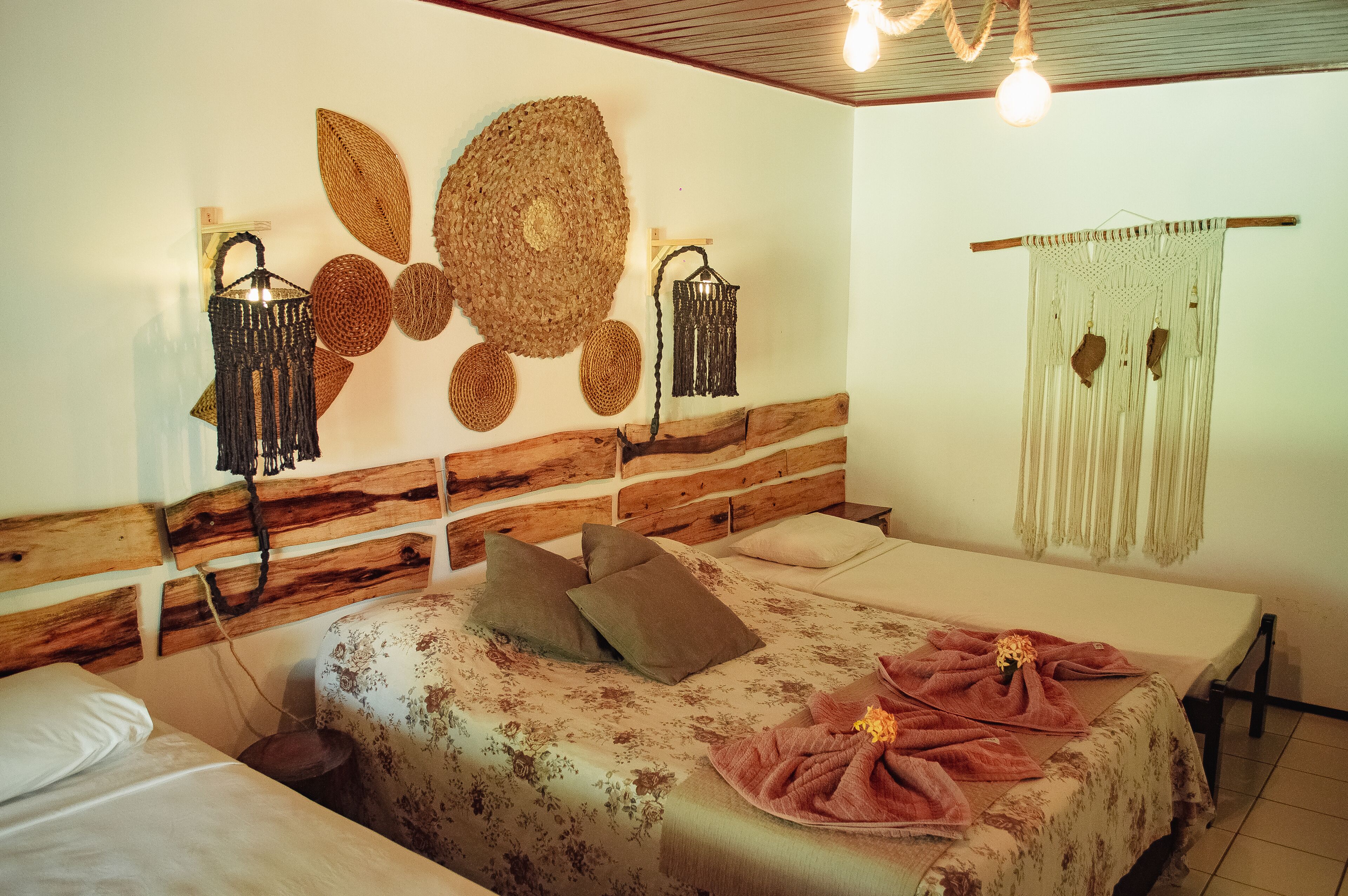A bedroom with a wooden headboard, two beds, a woven wall hanging, and a macrame curtain.