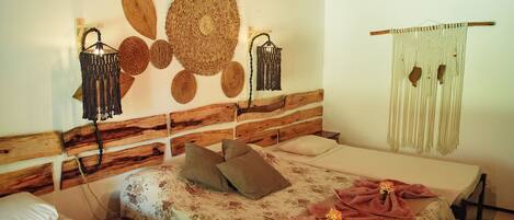 A bedroom with a wooden headboard, two beds, a woven wall hanging, and a macrame curtain.