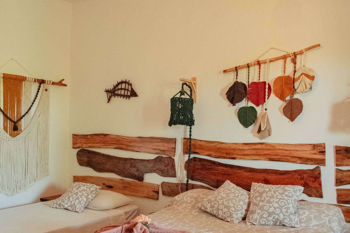 A bedroom with two beds, a wooden headboard, a hanging light fixture, and a wall hanging with leaves.