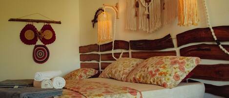 A bed with floral bedding, a wooden headboard, and a wall-mounted macrame light fixture.