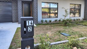 Una casa moderna de dos pisos con garaje, número 14, y un jardín delantero bien cuidado con plantas pequeñas y un sendero.
