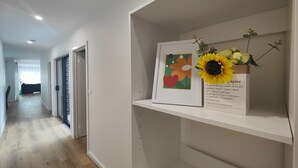 Un pasillo con un cuadro enmarcado y un florero con girasoles sobre una estantería.