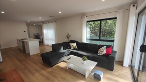 Una sala moderna con un sofá negro, una mesa de centro blanca y una cocina al fondo.