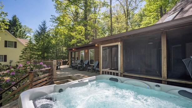 A hot tub surrounded by a wooden deck, outdoor seating, and a screened porch.