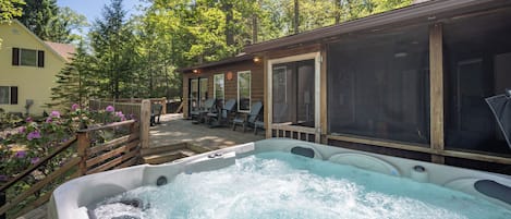 Un jacuzzi rodeado por una terraza de madera, asientos exteriores y un porche cubierto.