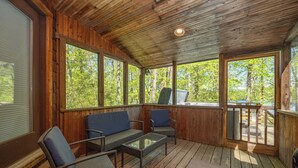A covered outdoor seating area with wicker furniture and large windows.