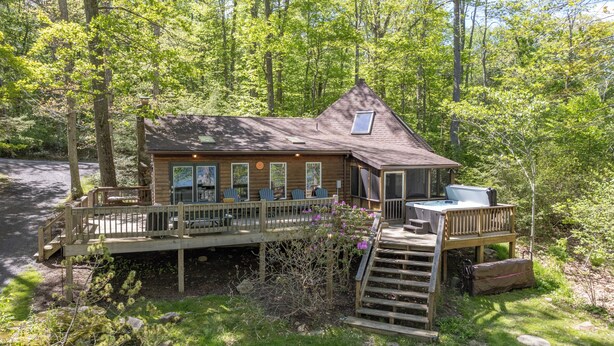 A cabin with a deck, a hot tub, and a staircase leading to a second level.