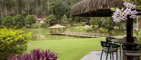 A patio with a thatched roof, a wooden deck, and a view of a lake and forest.