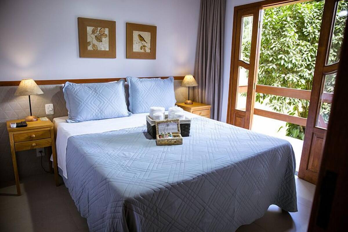 A hotel room with a large bed, two bedside tables, a nightstand, and a window with a view of greenery.