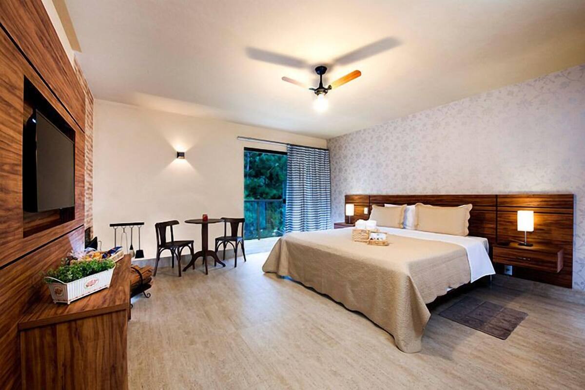 A hotel room with a bed, a TV, a desk with chairs, and a window with blinds.