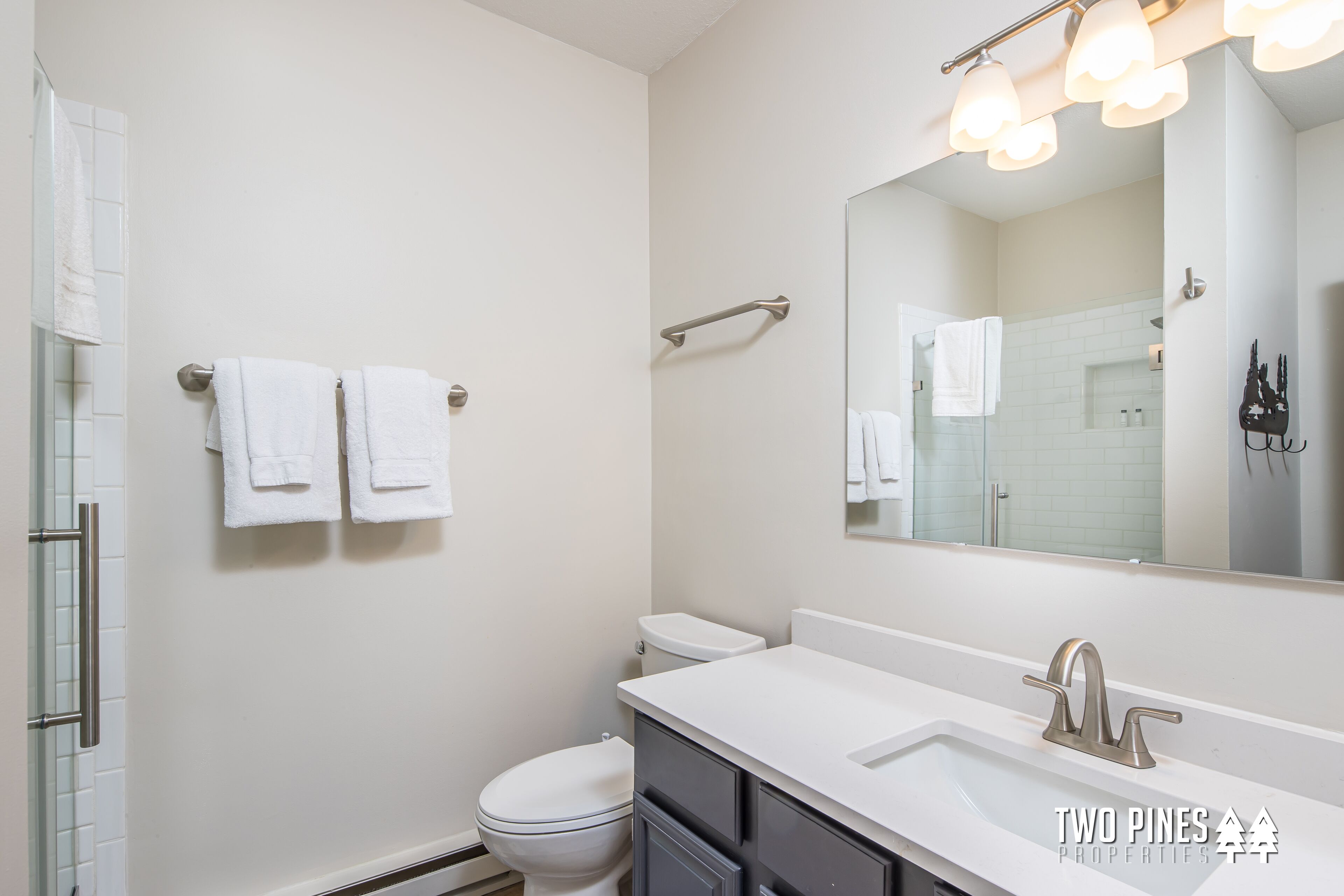 A modern bathroom with a white sink, a large mirror, and a toilet. There are two towels hanging on a towel rack.