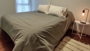 Ein Schlafzimmer mit Bett, Nachttisch, Lampe und einem Fenster mit Vorhängen.