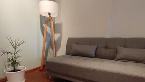 Ein modernes Wohnzimmer mit grauem Sofa, einer Stehlampe und einer Topfpflanze.