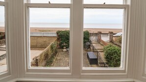 Udsigt gennem et vindue af en balkon med udsigt over stranden og en indhegnet have.