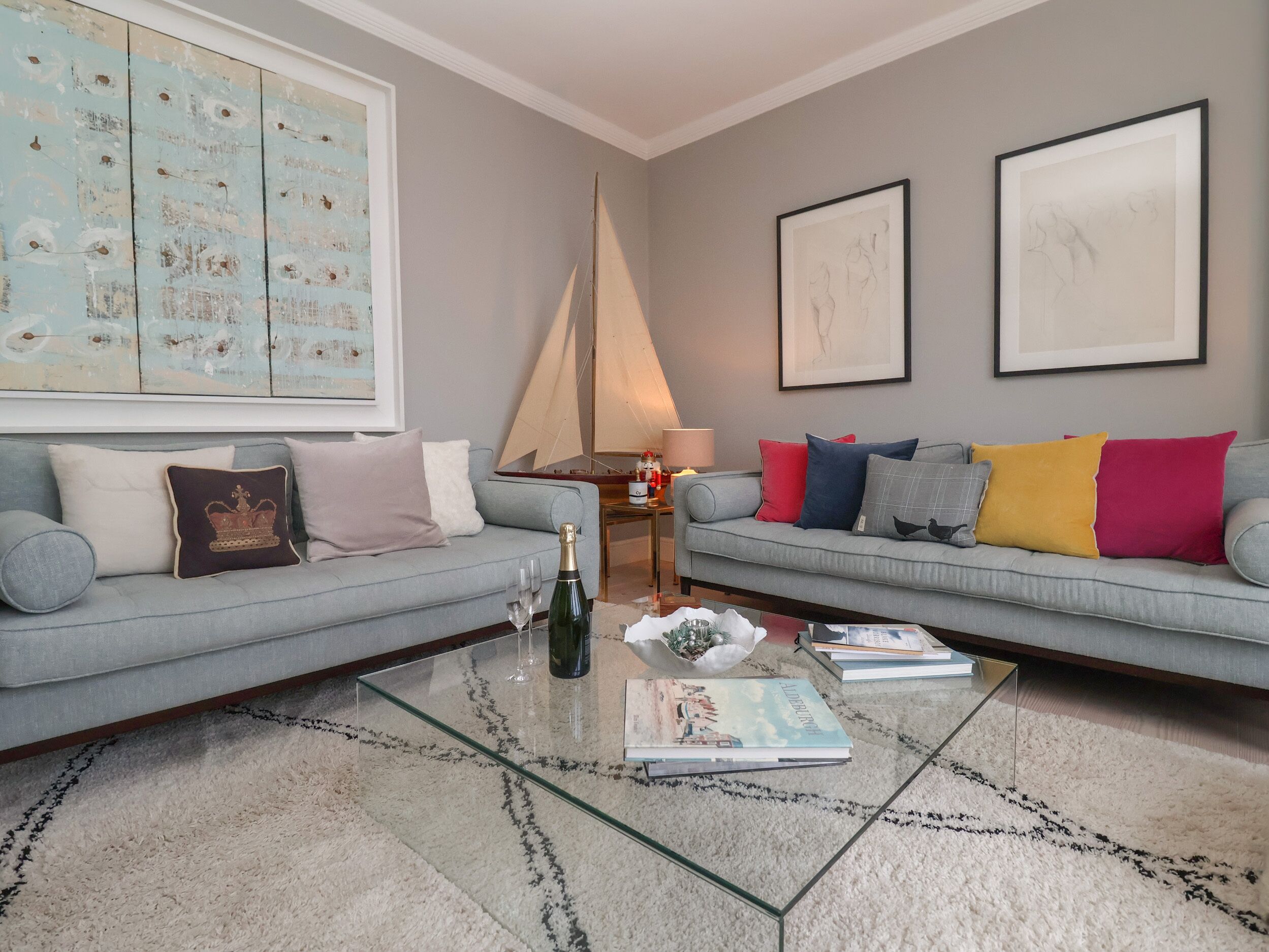 A living room with two grey sofas, a glass coffee table, and a large abstract painting on the wall.