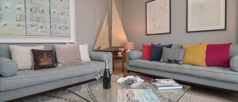 A living room with two grey sofas, a glass coffee table, and a large abstract painting on the wall.