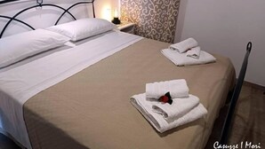 A neatly made bed with white linens, a beige bedspread, and two folded towels with a red rose.
