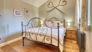 Un dormitorio con estructura de cama metálica, mesita de noche de madera, radiador y decoración en la pared.