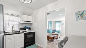 A compact kitchen with white cabinets, a black stove, and a window with blinds.