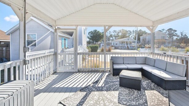 A covered outdoor deck with a sectional sofa and a patterned rug.