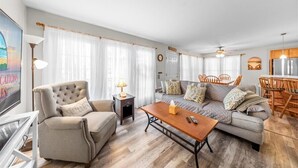 A living room with a sofa, armchair, coffee table, and a dining area with chairs and a table.