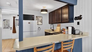 A kitchen with a bar counter, wooden chairs, a stove, and a hanging light fixture. - Ski-In/Ski-Out on Chair 8 | Cozy Condo Sleeps 6 (Brian Head)