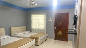 Une chambre d’hôtel avec deux lits, un ventilateur de plafond, une fenêtre avec des rideaux, une porte et un téléviseur posé sur un meuble.