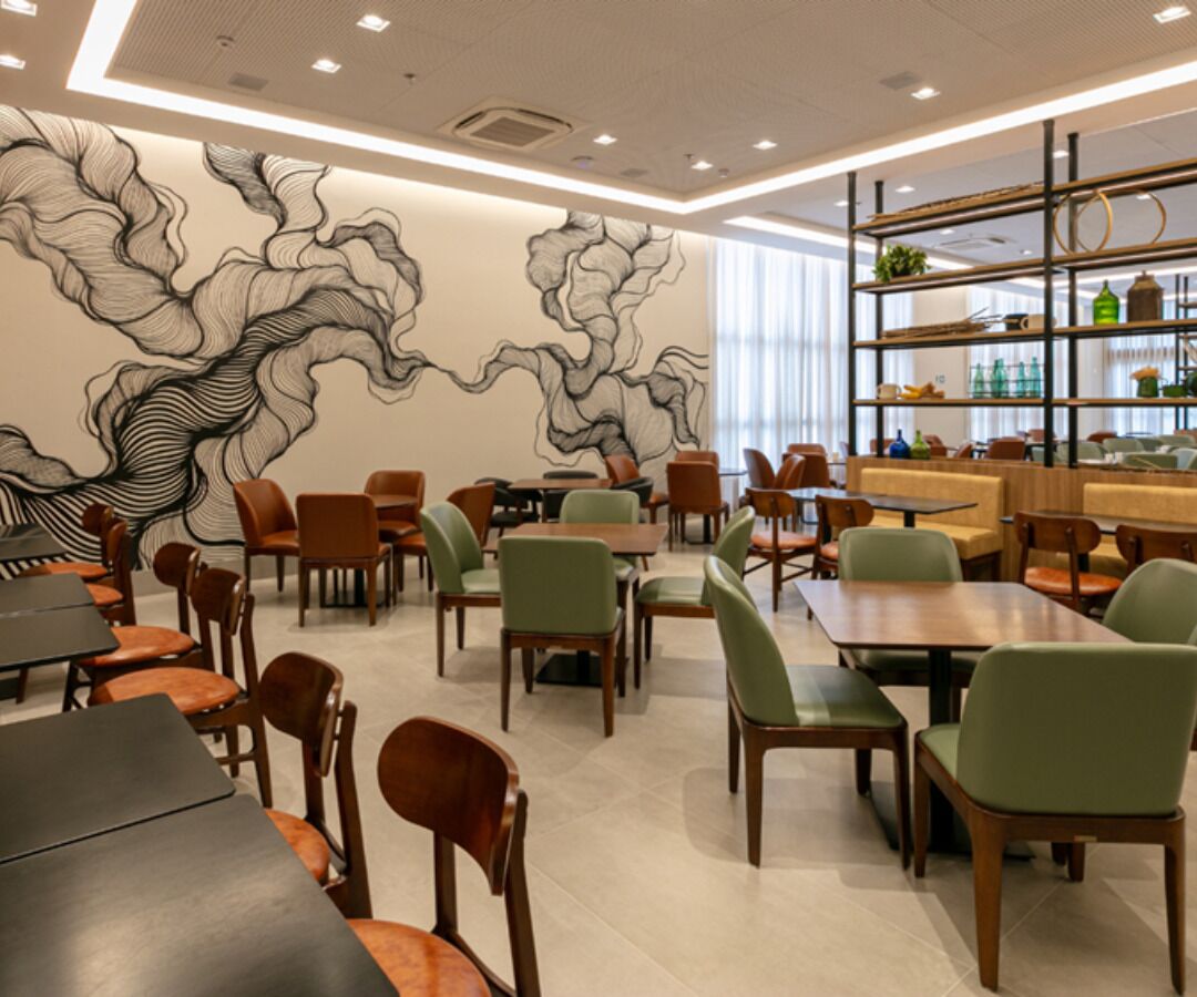 Interior moderno de restaurante con un mural central, mesas de madera y sillas verdes.