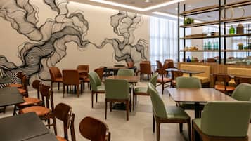 A modern restaurant interior with a central mural, wooden tables, and green chairs.