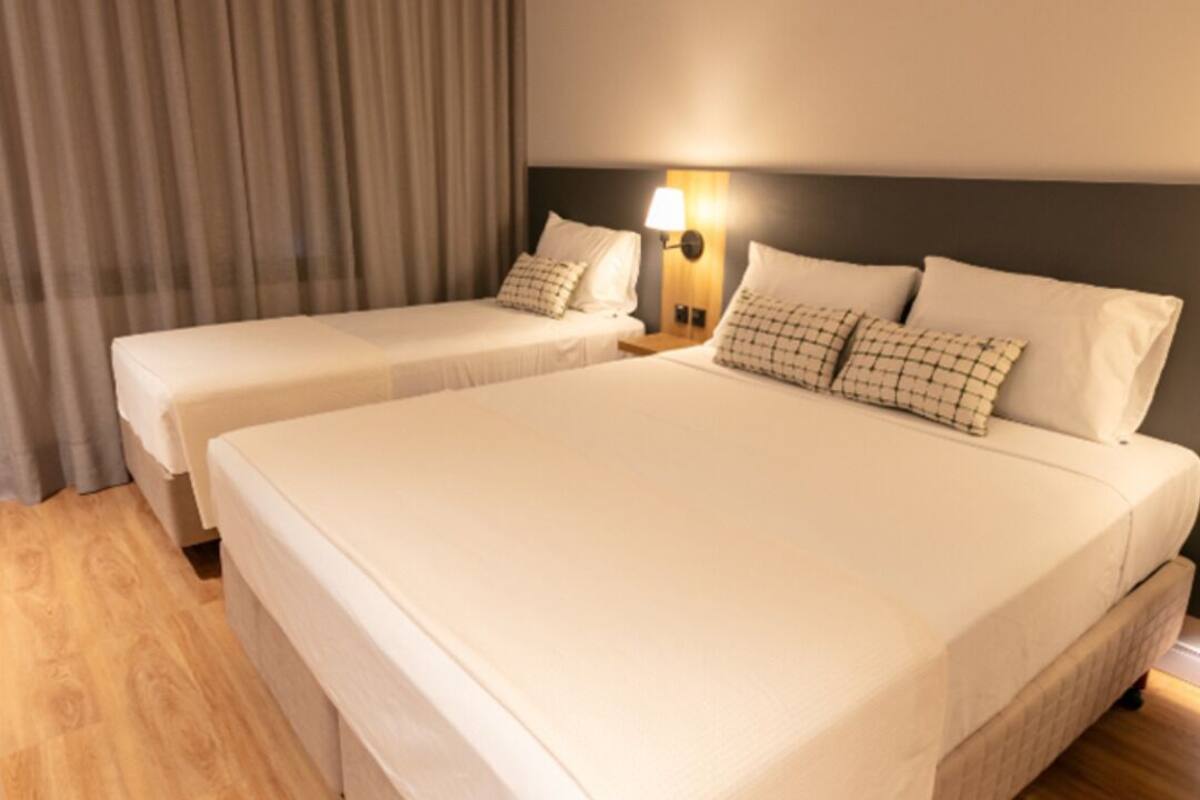 Una habitación de hotel con dos camas, piso de madera y una lámpara fijada a la pared.