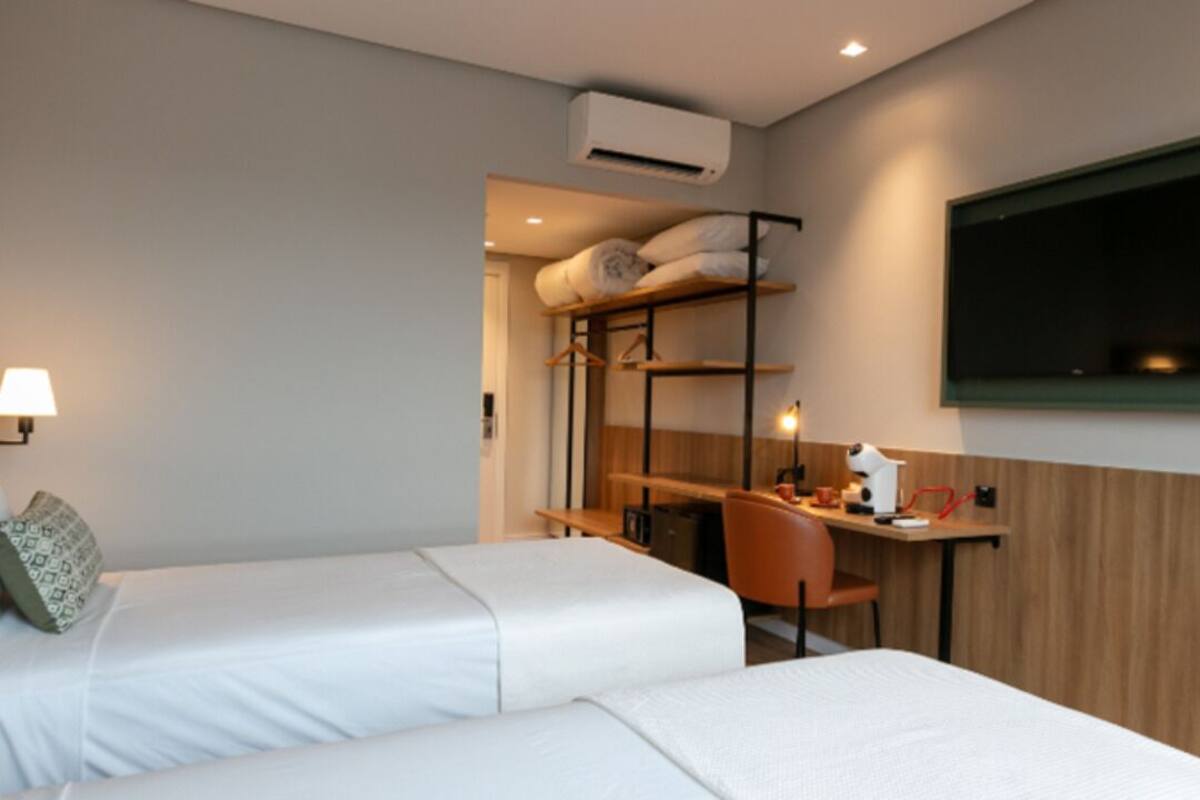 Habitación de hotel con dos camas, un escritorio, una silla y un televisor montado en la pared.